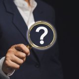 ハテナマークが書かれた虫眼鏡を向けるスーツの男性
